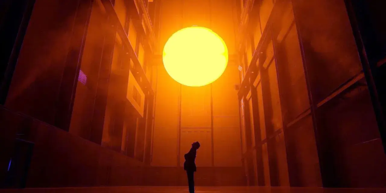 Une personne contemple un soleil artificiel dans l'installation "The Weather Project" d'Olafur Eliasson, baignant l'espace d'une lumière orangée intense.