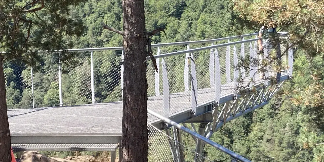 La passerelle himalayenne de Grazac offre une vue imprenable sur la vallée verdoyante. Une personne marche sur la structure métallique.