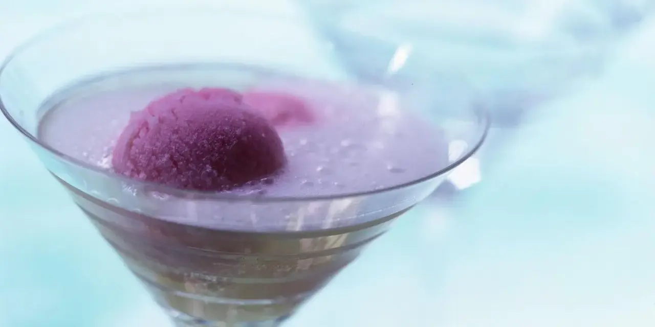 Ein erfrischendes Eis mit Sekt in einem Martiniglas. Die pinke Eiskugel schwimmt in prickelndem Sekt, ein Genuss für heiße Tage.