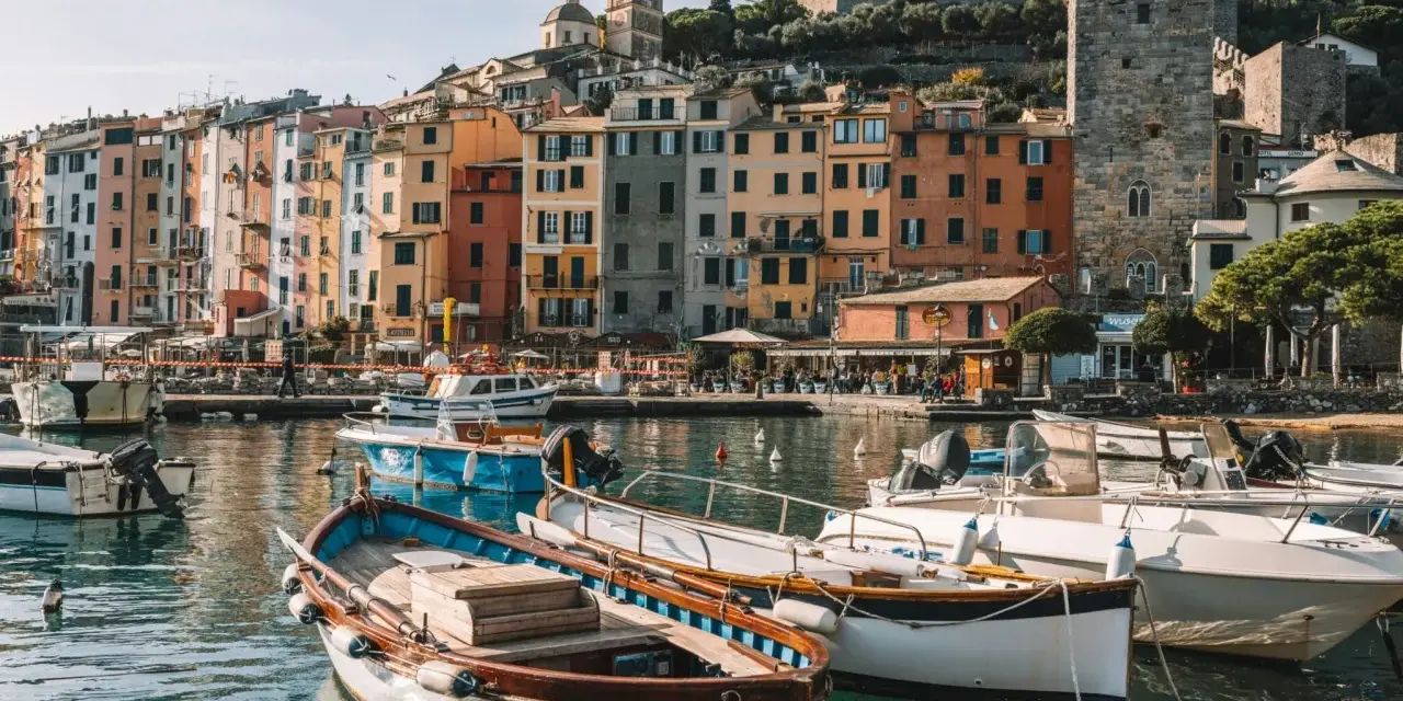 Boats bob in the harbor of a colorful Italian Riviera town, with ancient castles overlooking the vibrant buildings.