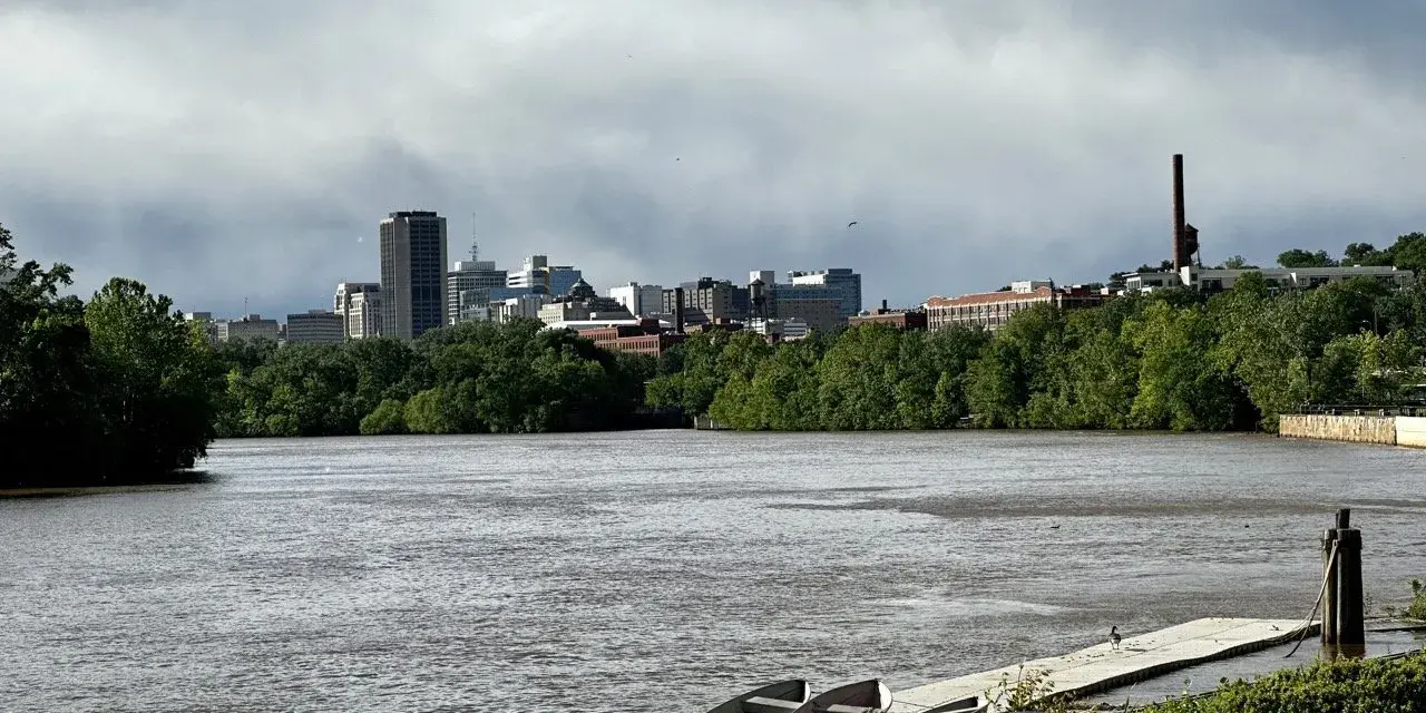 A cloudy sky looms over the Richmond, VA skyline, with the James River in the foreground. This view hints at fun things to do in Richmond, VA, like kayaking or enjoying the riverfront.