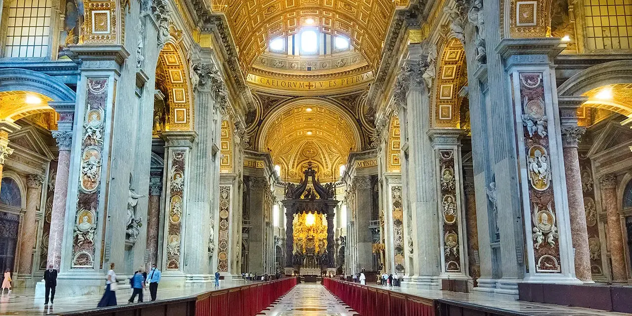 Interior of a grand basilica in Rome, with ornate golden ceilings, marble columns, and a long aisle lined with red velvet.
