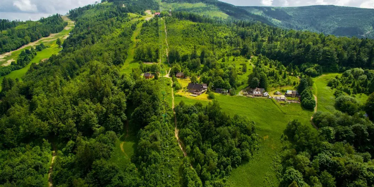 Widok z lotu ptaka na zielone wzgórza Beskidu Śląskiego ze szlakami i domkami.