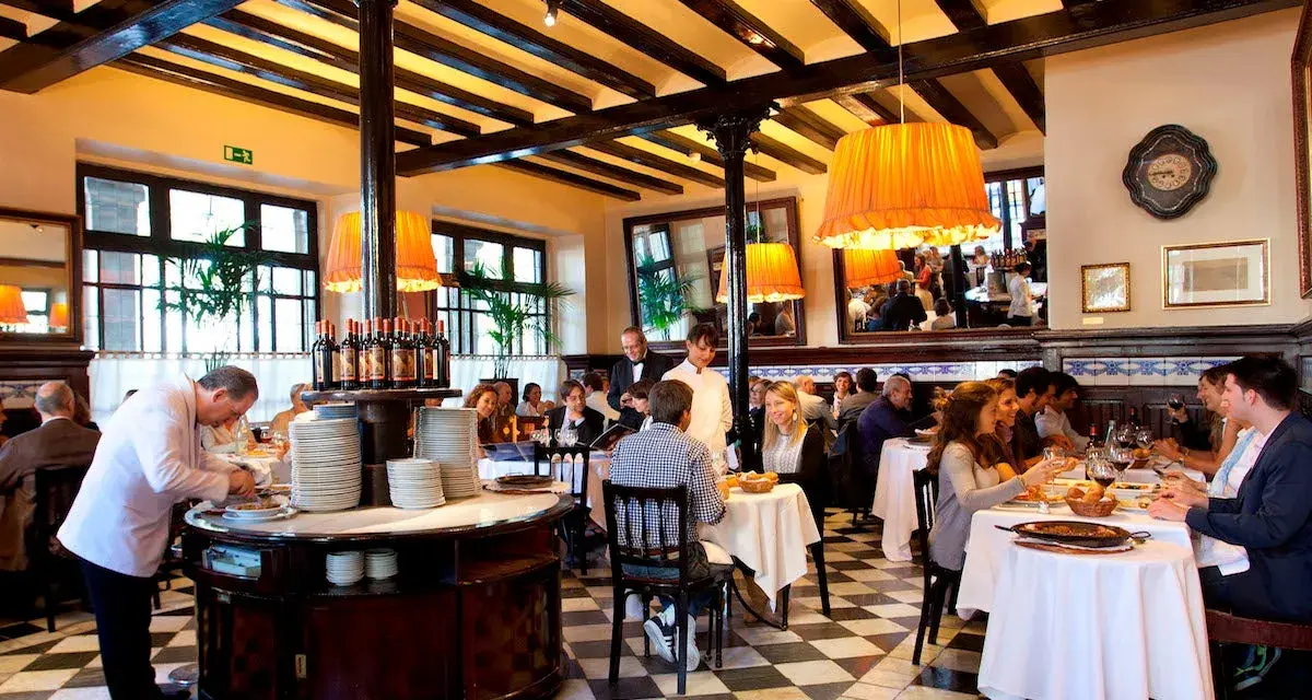 Un camarero prepara platos en un restaurante lleno de comensales. Los pasos para abrir un restaurante incluyen crear un ambiente acogedor como este.