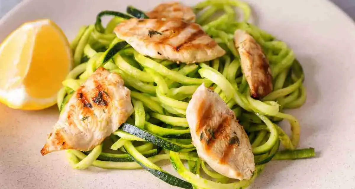 Spaghetti di zucchine con straccetti di pollo grigliato e una fetta di limone.