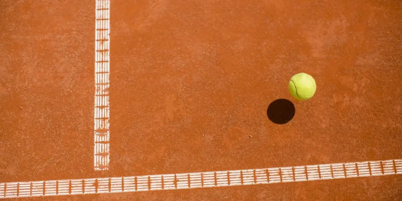 Piłka tenisowa na ceglanej nawierzchni, tuż obok linii bocznej. Czy to decydujący punkt za Roland Garros?