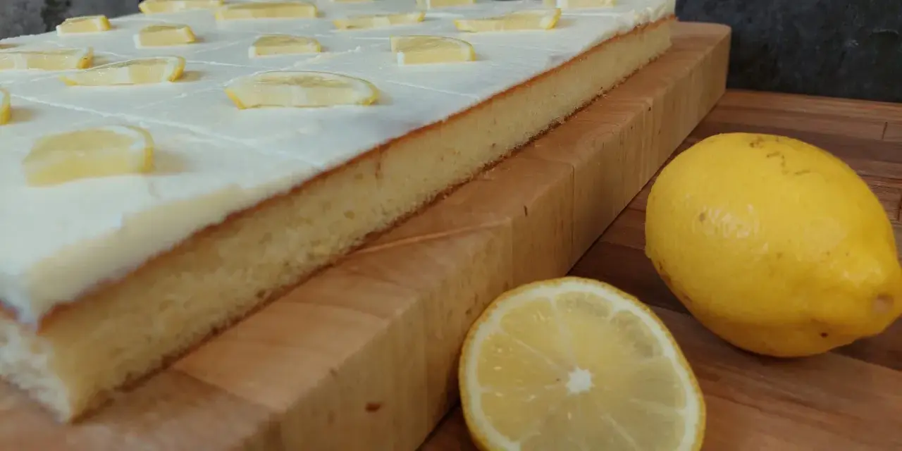 Ein saftiger sizilianischer Zitronenkuchen, bedeckt mit weißer Glasur und Zitronenscheiben, daneben frische Zitronen.