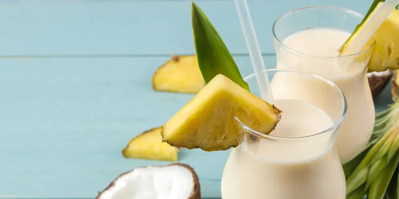 Dwa orzeźwiające koktajle pina colada z kawałkami ananasa i kokosem na niebieskim tle.