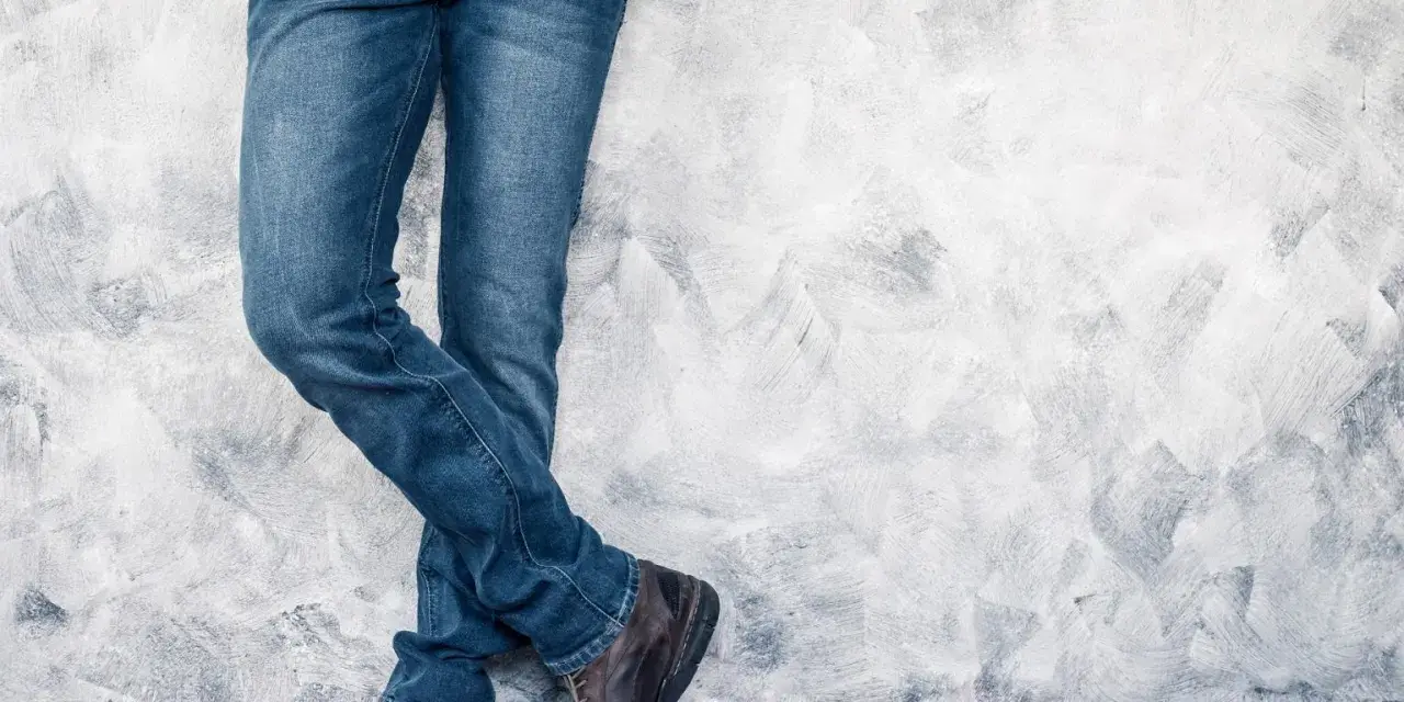 Mężczyzna w jeansach H&M, stojący przy ścianie. Rozmiarówka H&M wypada standardowo, idealnie dopasowana.