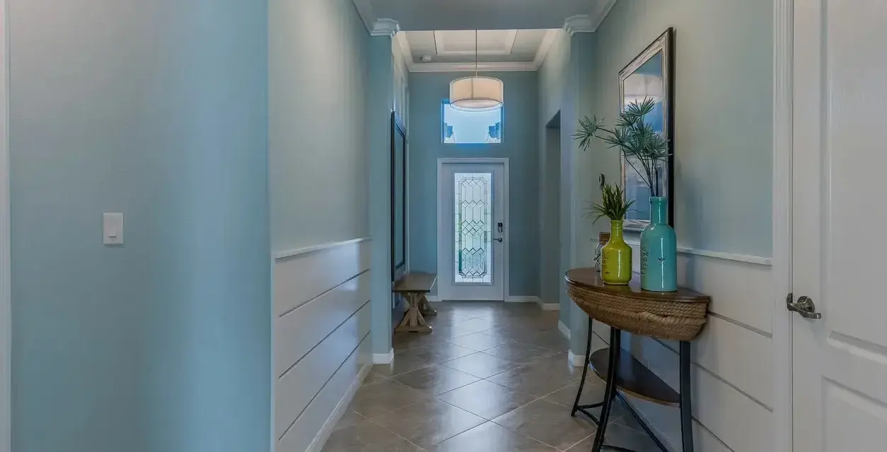 Un couloir lumineux avec une peinture de couloir 2 couleurs : bleu ciel et blanc. Un banc, une console avec des vases et une porte vitrée ornent cet espace accueillant.