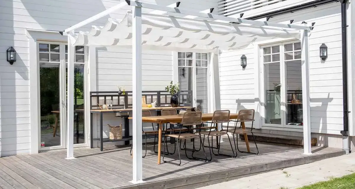 En vit pergola med tygtak skapar en mysig uteplats med matbord och stolar. Perfekt för att bygga pergola med plasttak för soliga dagar.