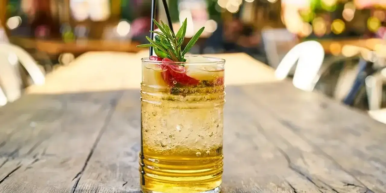 Orzeźwiający drink z plasterkami owoców i gałązką rozmarynu, idealny na letnie popołudnie. W szklance widać bąbelki, sugerujące, że to piwo gingers.