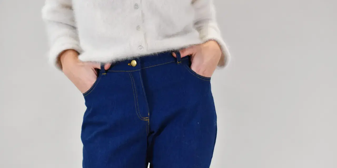 Gros plan sur une personne portant un pull blanc et un pantalon en jean bleu avec les mains dans les poches.
