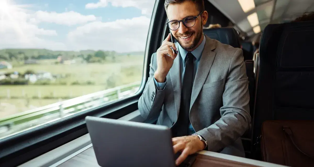 Biznesmen w garniturze rozmawia przez telefon i pracuje na laptopie w pociągu.