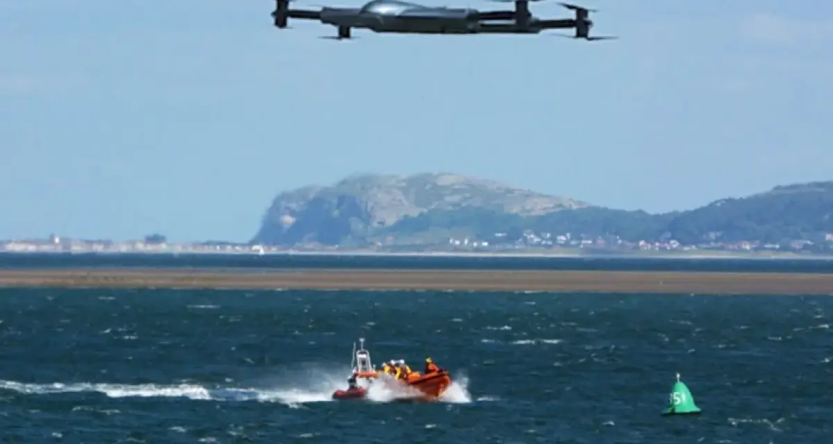 Search and rescue drones hover over a lifeboat speeding across choppy waters, assisting in a coastal operation.