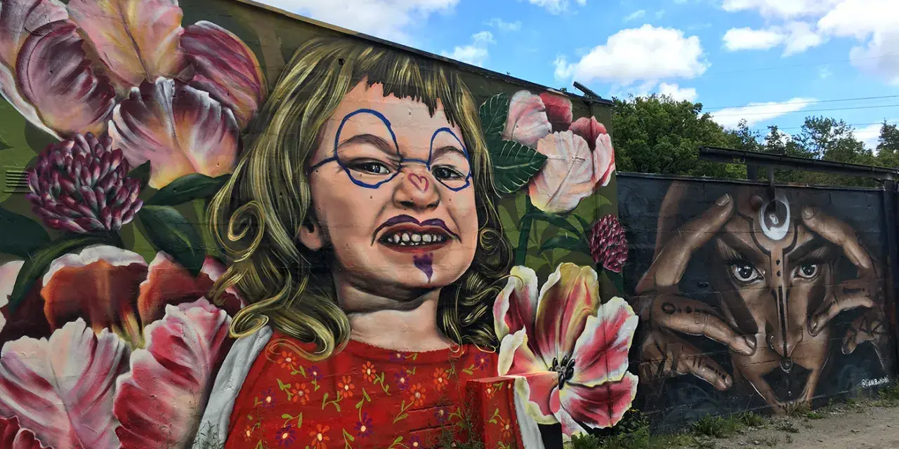 En väggmålning med en busig flicka omgiven av blommor ger graffiti inspiration. Bredvid syns ett mystiskt ansikte med händer.