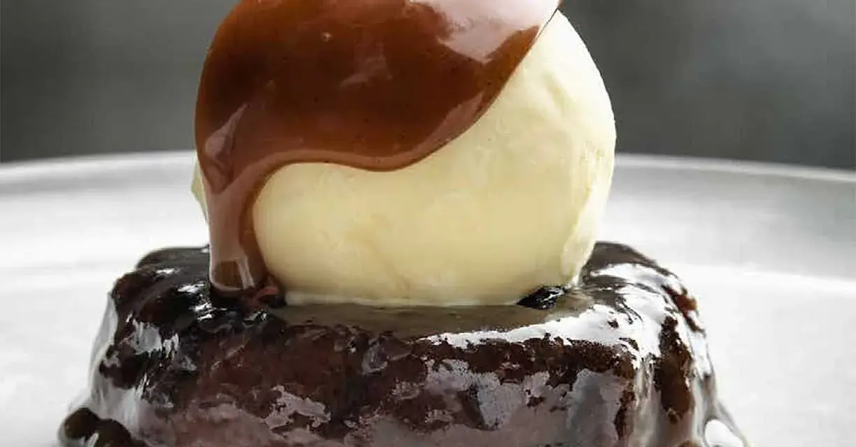 En läcker sticky toffee pudding med en kula vaniljglass och varm kolasås som rinner över.
