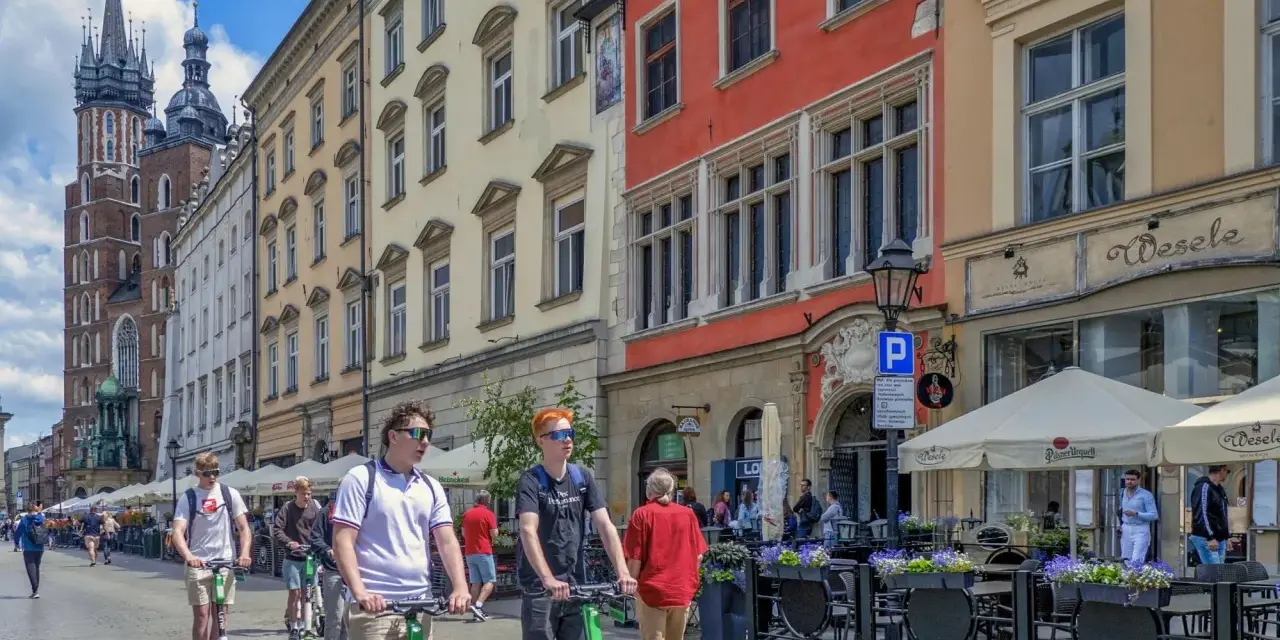 Młodzi ludzie na hulajnogach w Krakowie, idealne na city break. W tle Sukiennice i Kościół Mariacki.