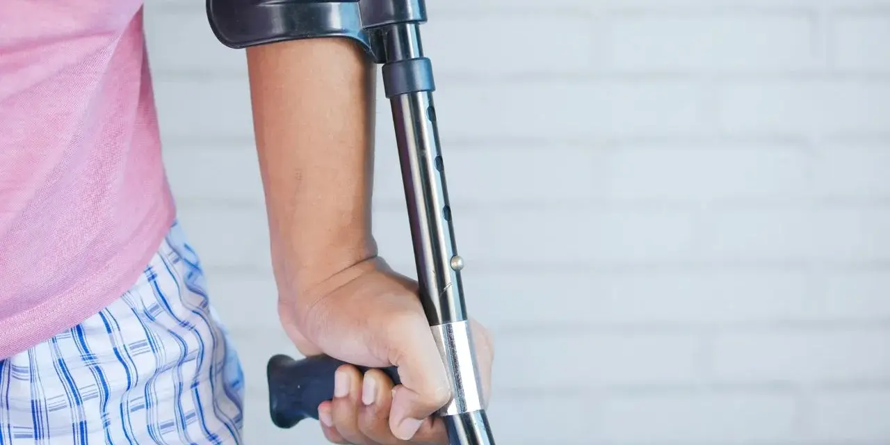 Osoba z kulą, być może po wypadku, który mógłby być opisany jako art. 156 kk. Różowa koszulka i kratkowane spodenki.
