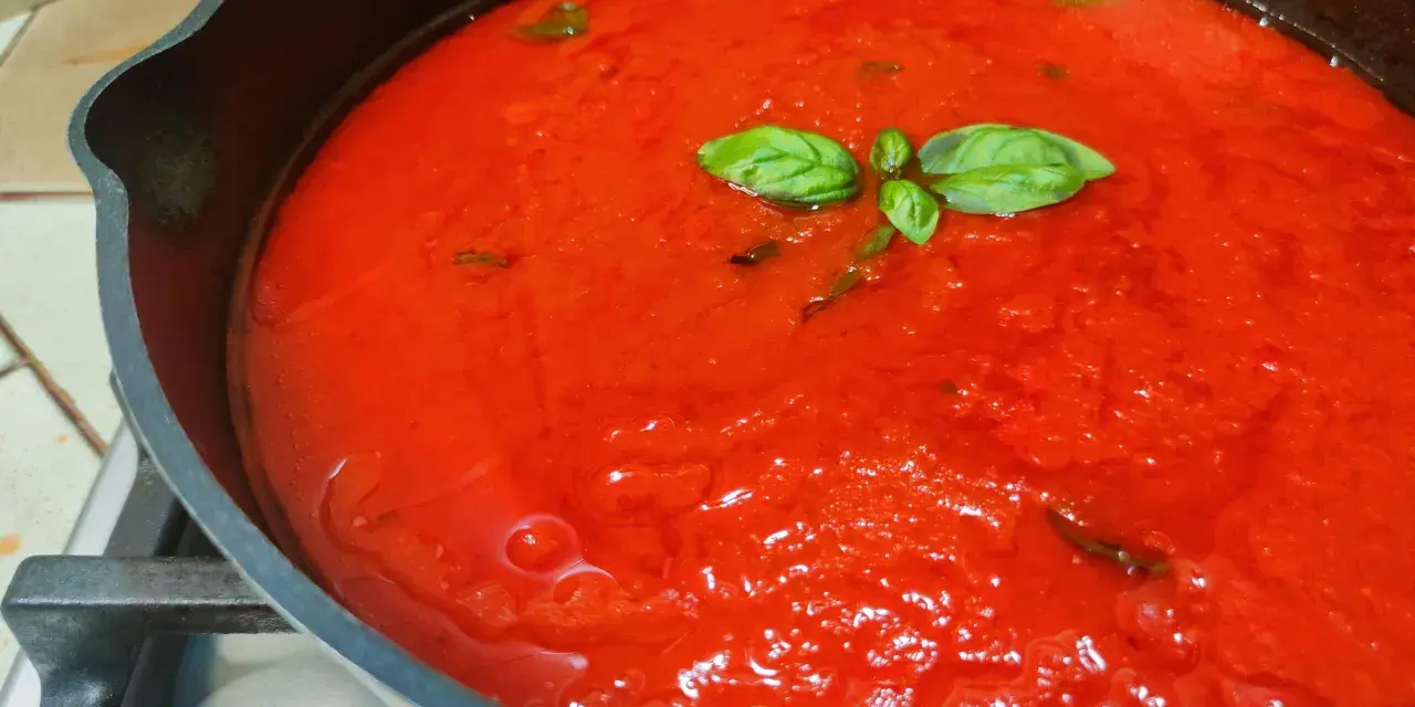 Sugo al pomodoro fresco e profumato, con foglie di basilico che galleggiano in una padella di ghisa.