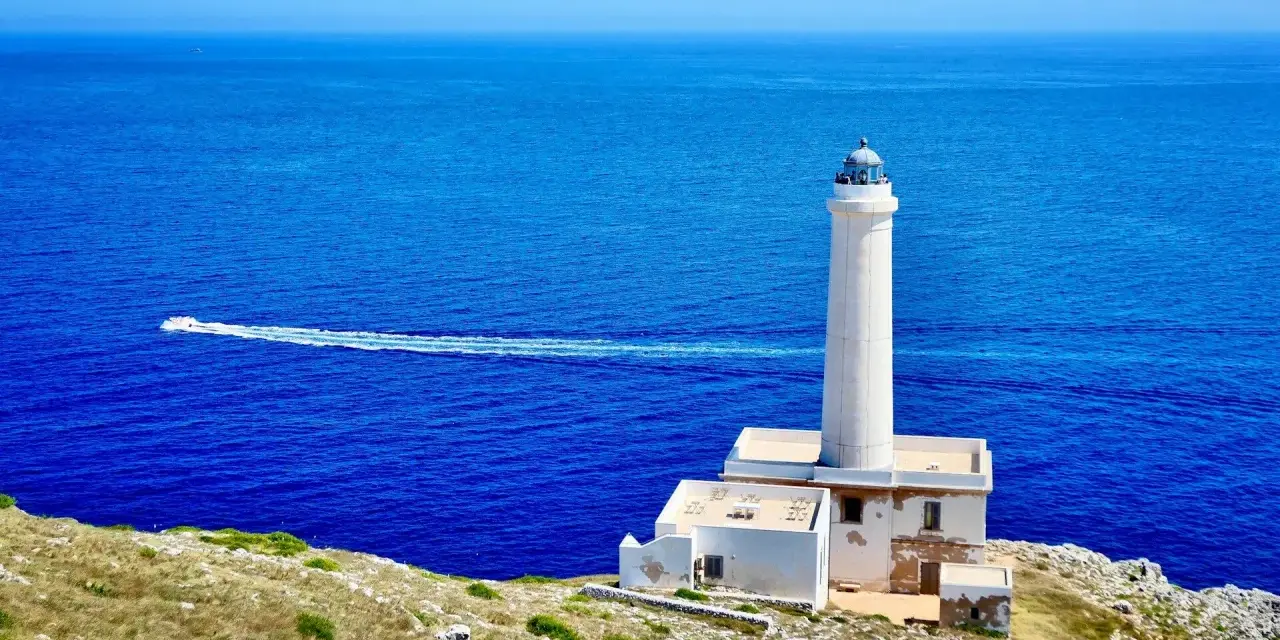 Faro di Punta Palascìa, uno dei luoghi da vedere a Otranto, con il mare blu e una barca in lontananza.