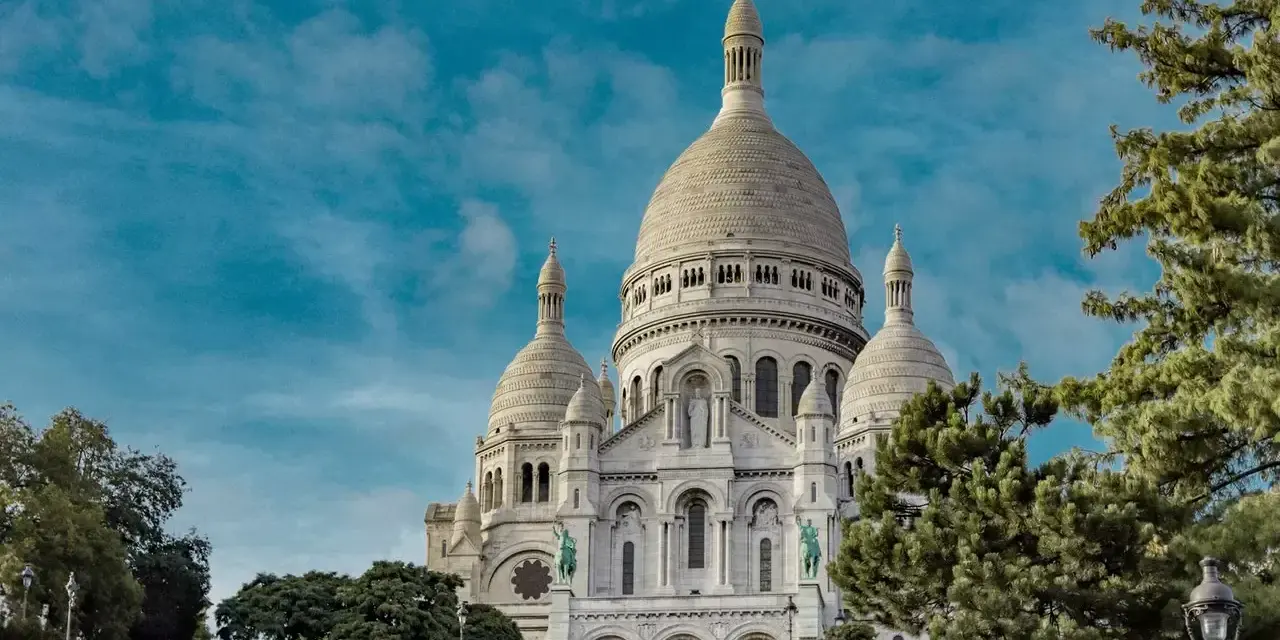 Basílica del Sacré-Cœur, uno de los monumentos de Francia, se alza majestuosa bajo un cielo azul con nubes.