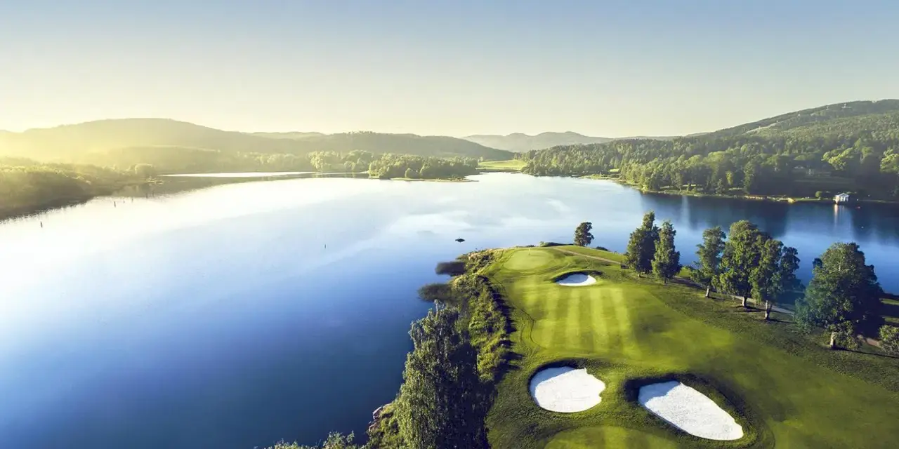 Vacker golfbana vid en sjö, perfekt för norsk golf. Grönskande kullar och solnedgång.
