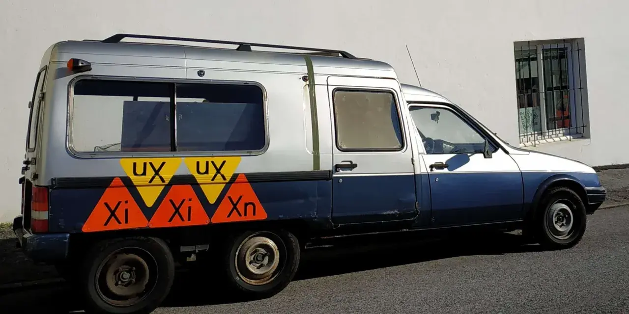 Dwukolorowy Citroen C15 z nietypowymi oznaczeniami "UX" i "Xi Xn" na boku, zaparkowany przy białej ścianie.