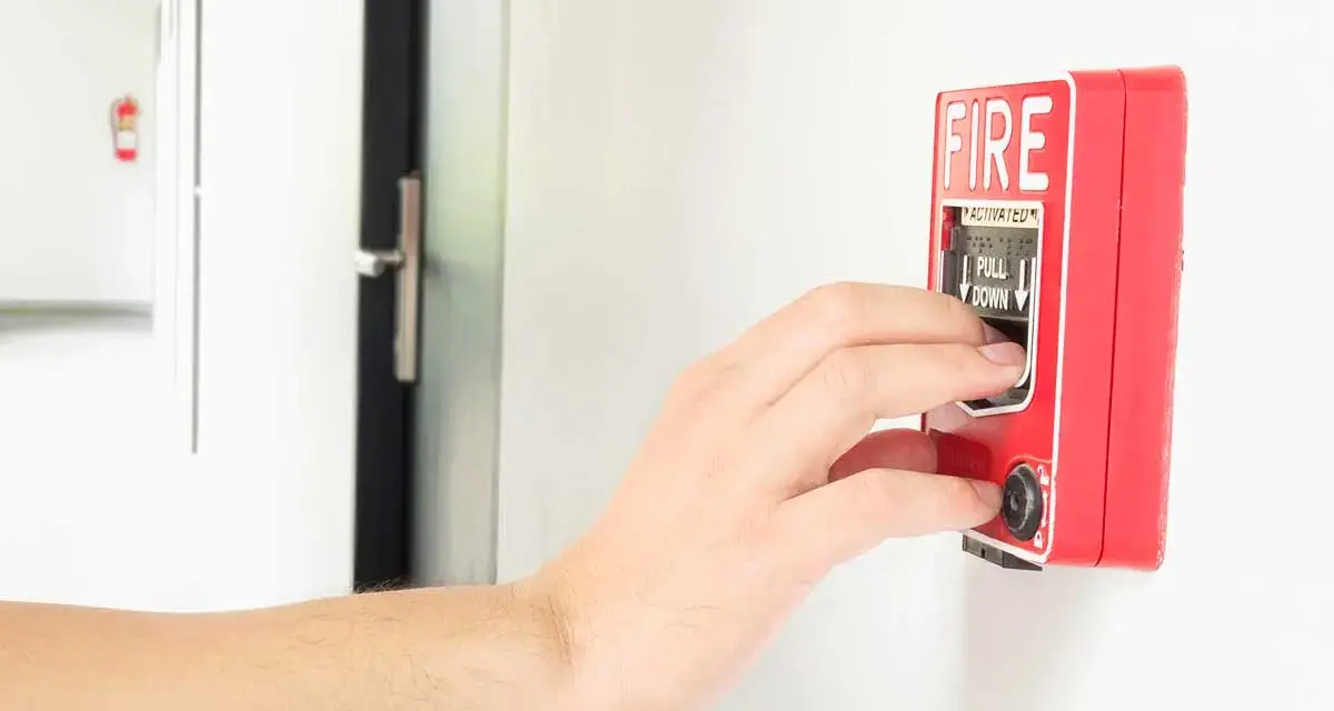Mano activando la alarma de incendios. Instrucciones claras: "PULL DOWN" para saber cómo apagar alarma de incendios.