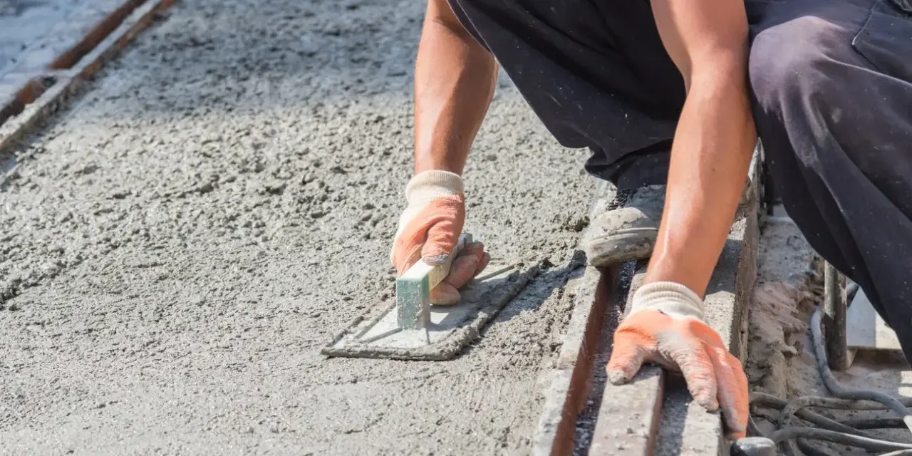 Pracownik wygładza świeży beton, dbając o odpowiednie suchy beton proporcje. Ręce w rękawiczkach trzymają kielnię.