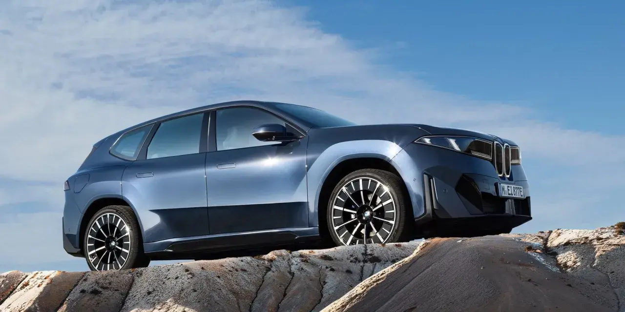 Niebieskie BMW iX3 na tle błękitnego nieba, stojące na skalistym podłożu.