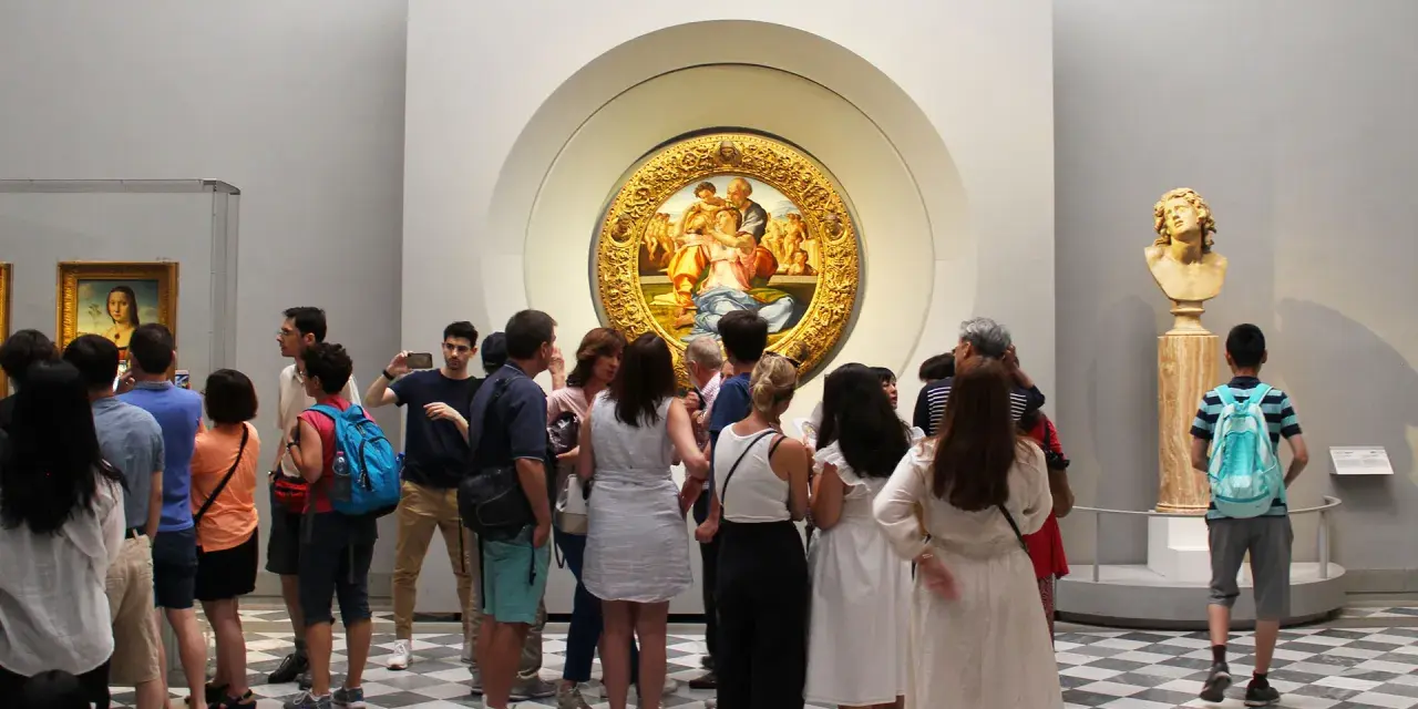 Galeria Uffizi: co zobaczyć? Grupa turystów podziwia okrągły obraz w złotej ramie i rzeźbę.