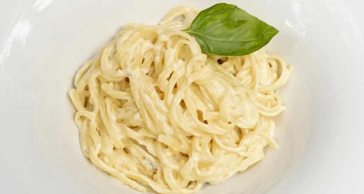 Un plato de spaghetti a la carbonara con nata, cremoso y adornado con una hoja de albahaca fresca.