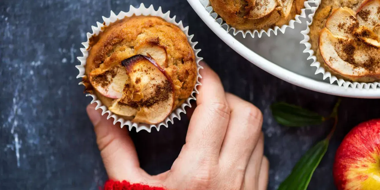 Hand hält einen frisch gebackenen Apfelmuffin, bestreut mit Zimt. Ein tolles Apfelmuffins Rezept!