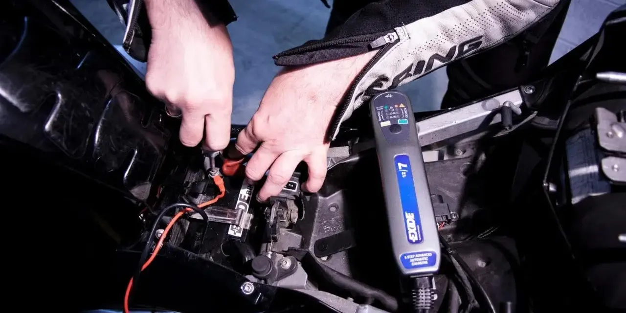 Mani che collegano un caricabatterie Exide alla batteria di una moto, per risolvere il problema della batteria si scarica a moto ferma.