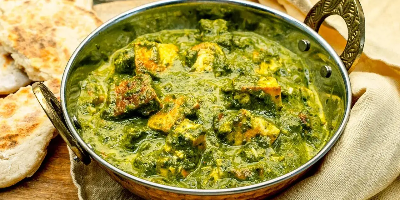 Ein köstliches Palak Paneer in einer Kupferschale, serviert mit Fladenbrot und Chiliflocken.