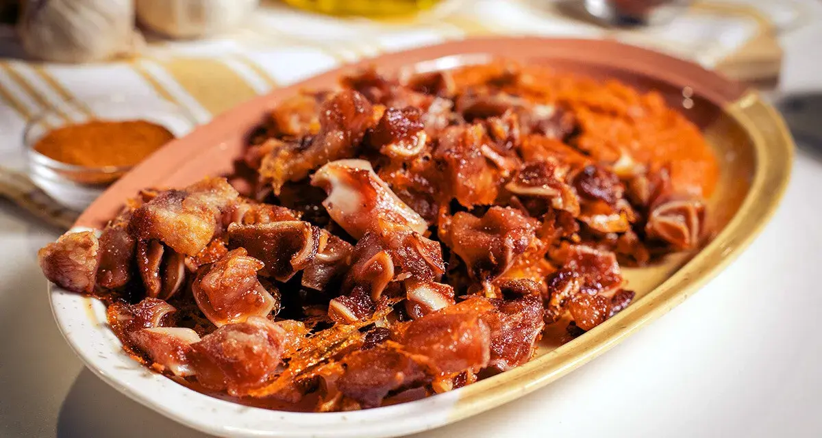 Oreja de cerdo crujiente y dorada servida en un plato con puré naranja.