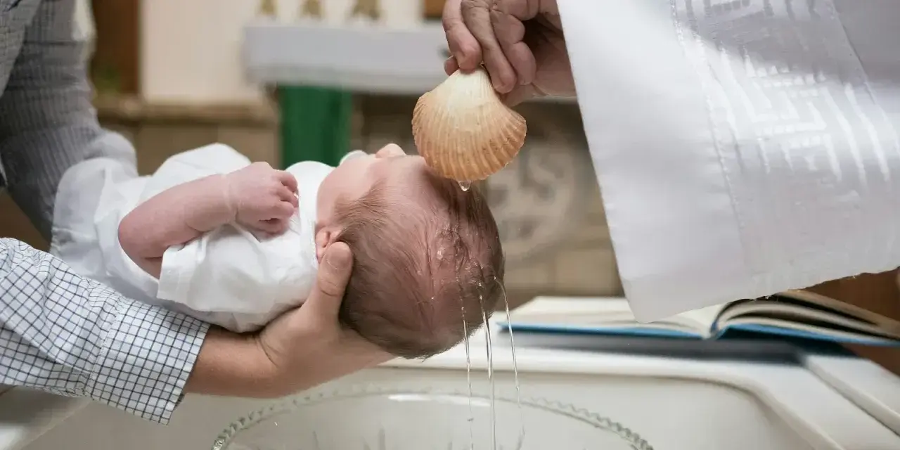 Chrzestna polewa główkę dziecka wodą święconą z muszli podczas ceremonii chrztu.