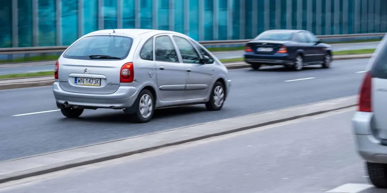 Srebrny Citroën Xsara Picasso jedzie po drodze, mijając inne samochody.