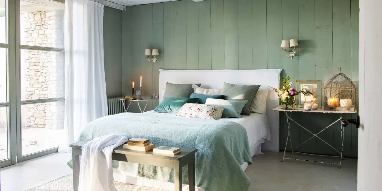 Acogedor dormitorio verde agua y blanco con cama mullida, cojines y luz natural.