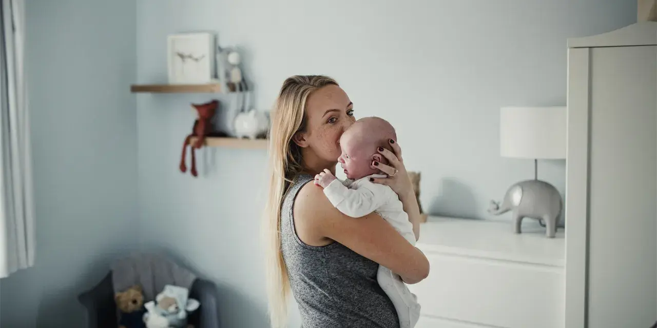 Mama tuli tulula noworodka, kołysząc go czule. W tle pokój dziecięcy z pluszakami.