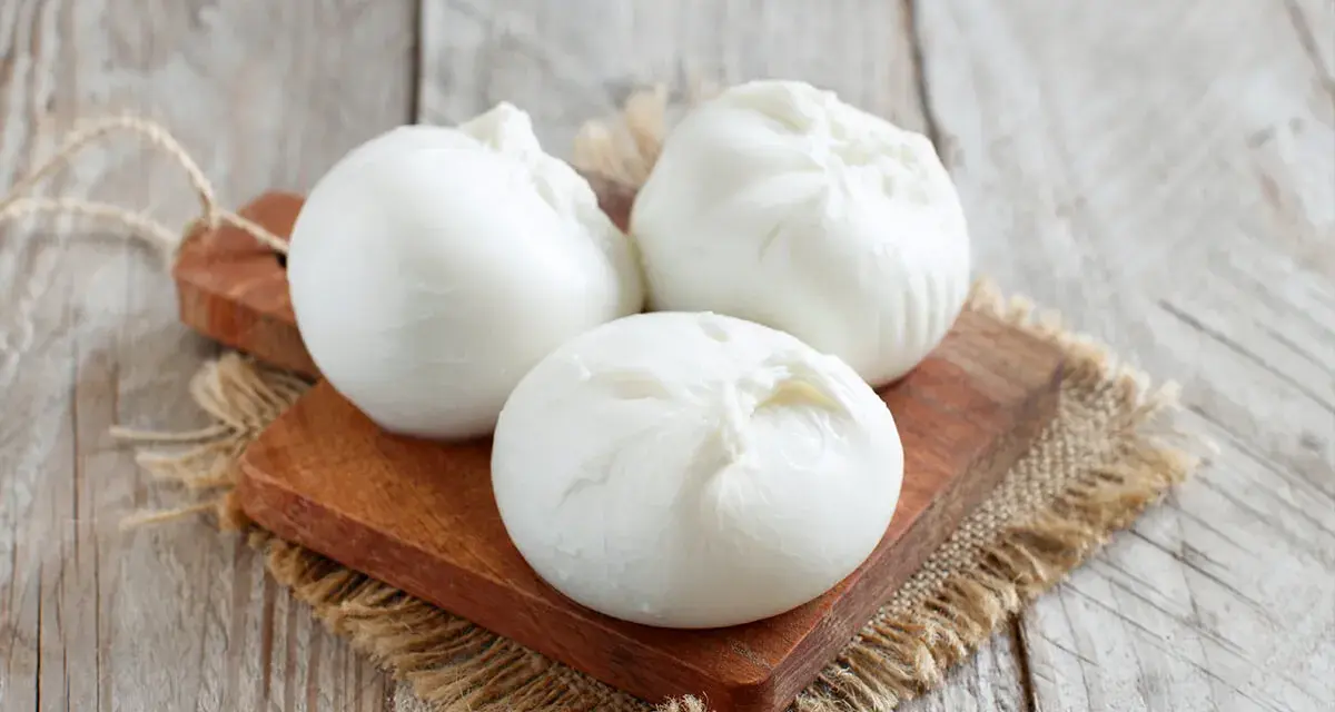 Trois boules de burrata crémeuse sur une planche en bois, parfaites pour comprendre la différence burrata et mozzarella.