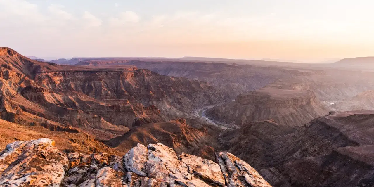 Wąwóz Fish River w Namibii, z rzeką wijącą się w dole. Zachodzące słońce maluje skały na ciepłe barwy.
