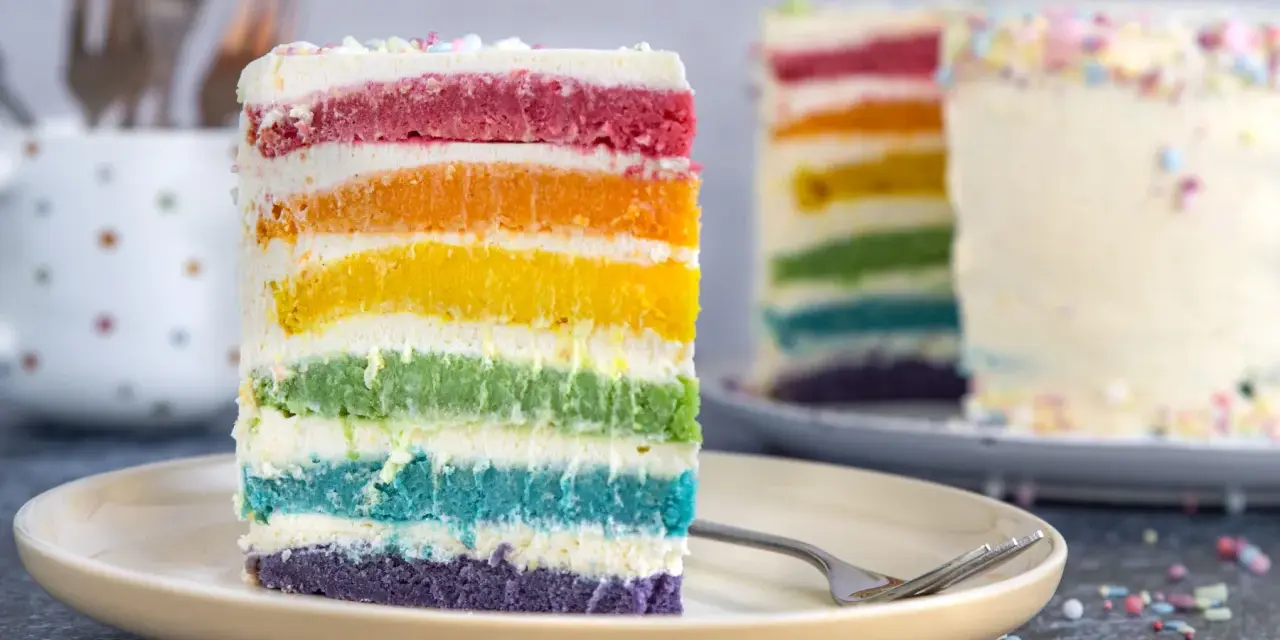 Ein Stück Regenbogen Kuchen mit bunten Schichten und Streuseln auf einem Teller.