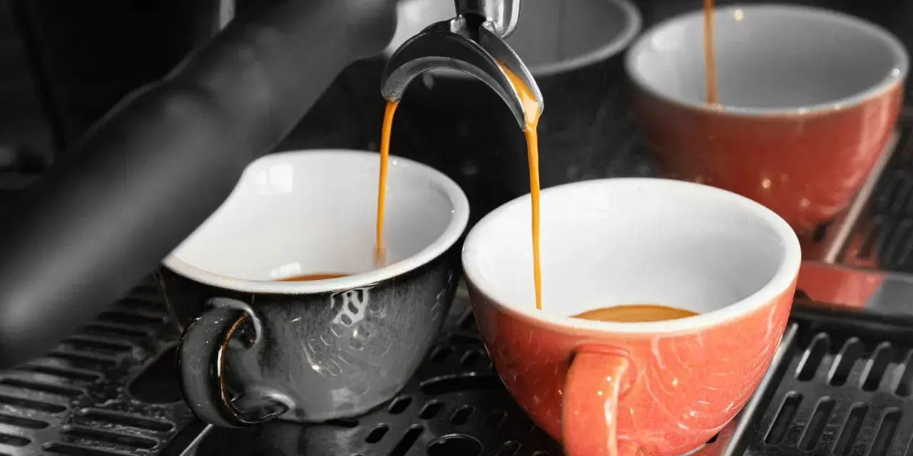 Dwie filiżanki, jedna szara, druga pomarańczowa, napełniają się aromatyczną kawą doppio.