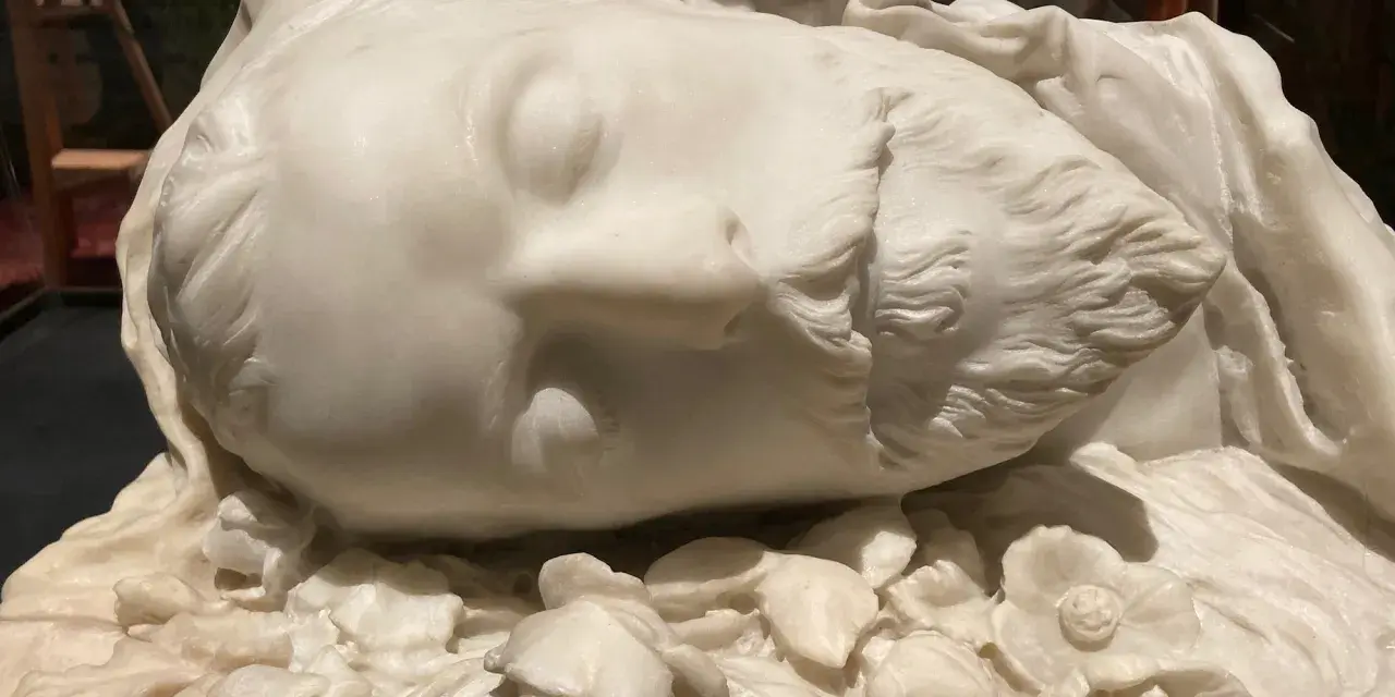 Sculpture en marbre d'un visage endormi, entouré de fleurs. Une œuvre d'art évoquant la célèbre Sarah Bernhardt.