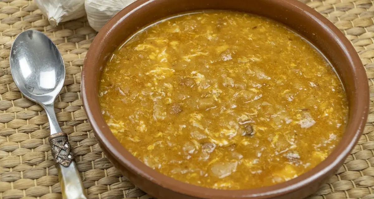 Sopa de ajo tradicional en cuenco de barro, con ajos y cuchara al lado.