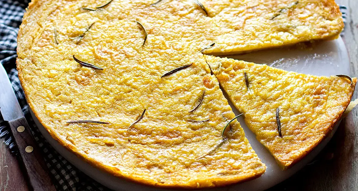 Una torta dorata, profumata al rosmarino, perfetta come ricetta con farina di ceci. Una fetta è già stata tagliata.
