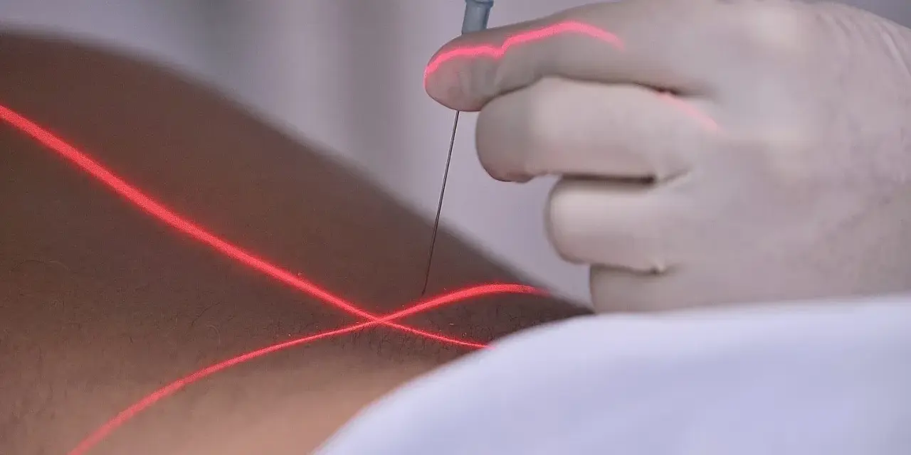 Eine Hand in einem Handschuh führt eine prt spritze unter rotem Laserlicht.