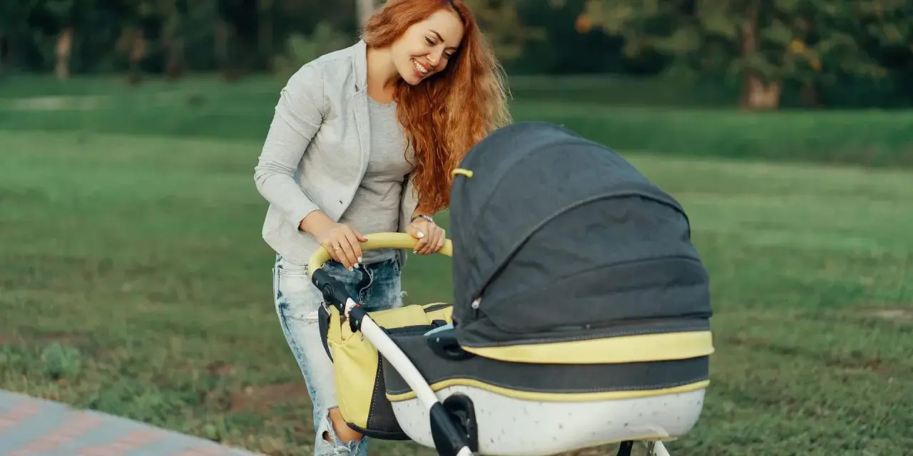 Mama z rudymi włosami uśmiecha się do wózka. Idealny przykład, jak ubrać noworodka na spacer 15 stopni.